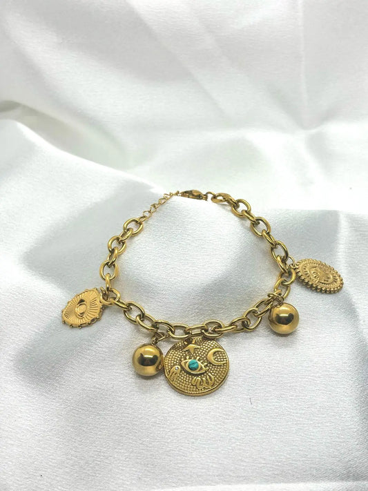 Bracelet doré à breloques sur tissu blanc.
