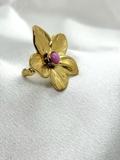 Bague fleur dorée femme avec pierre centrale rose portée sur fond blanc