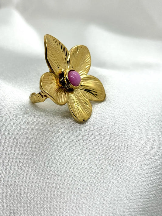 Bague fleur dorée femme avec pierre centrale rose portée sur fond blanc
