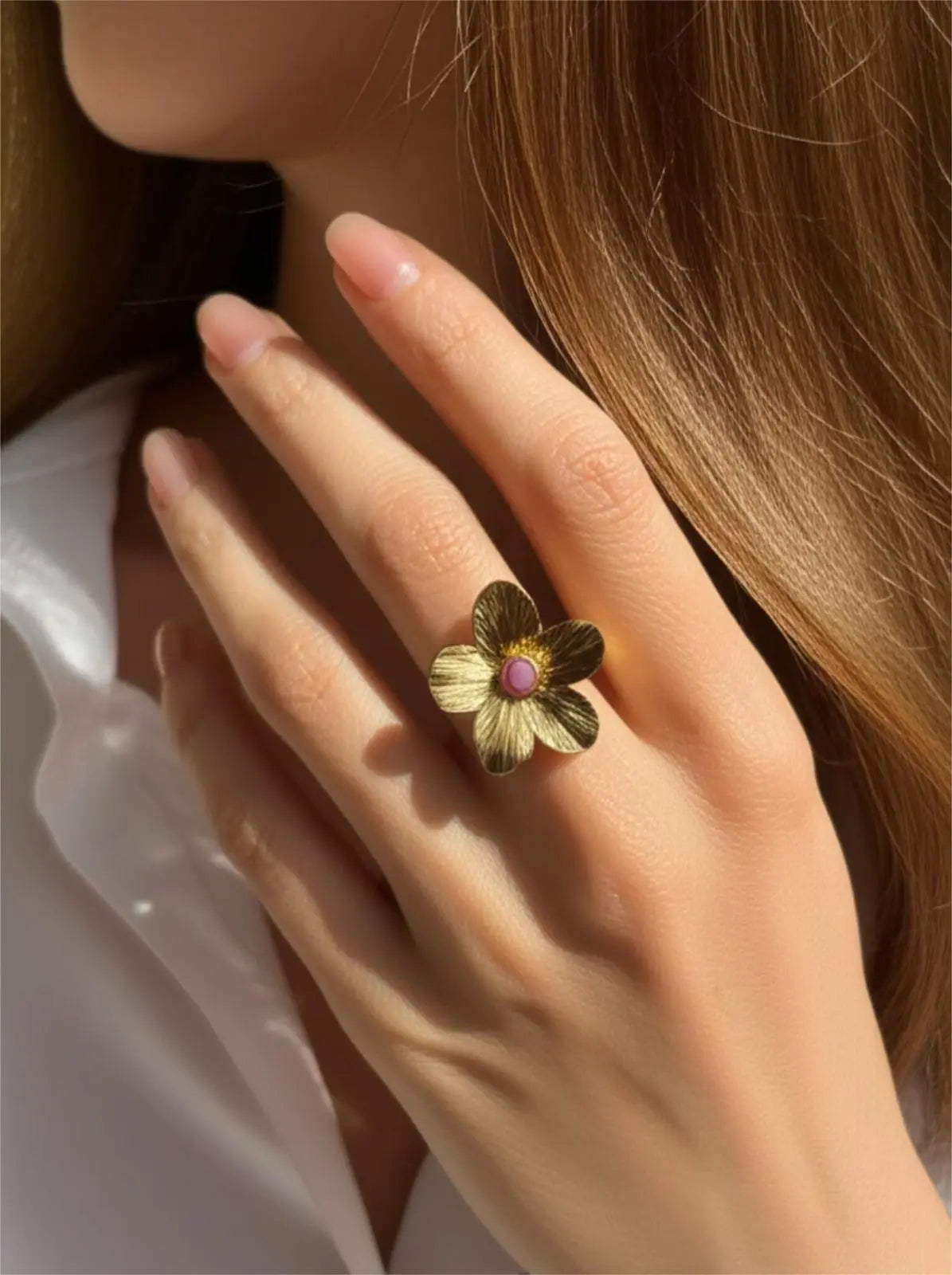Bague fleur dorée femme avec pierre rose portée sur la main d'une femme
