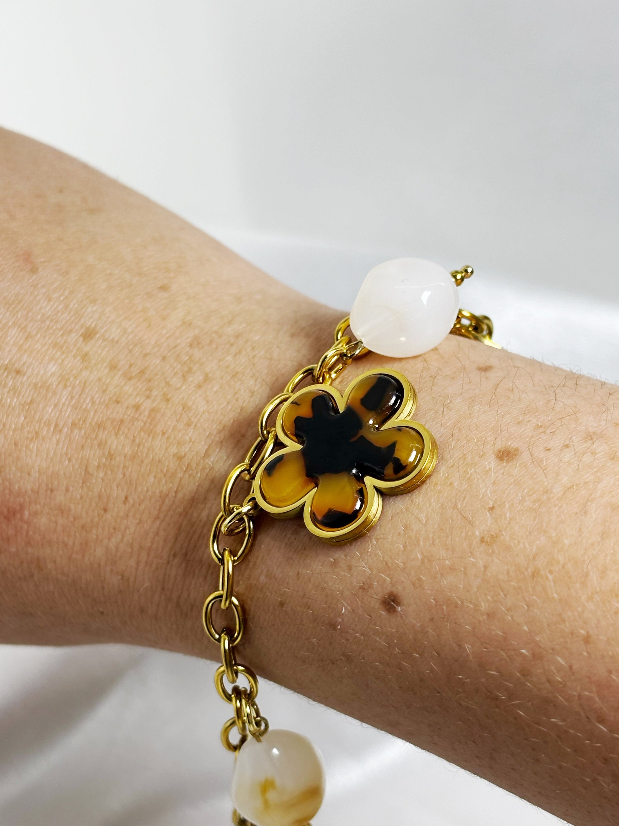 Bracelet doré avec charms en forme de fleur et pierres blanches porté au poignet