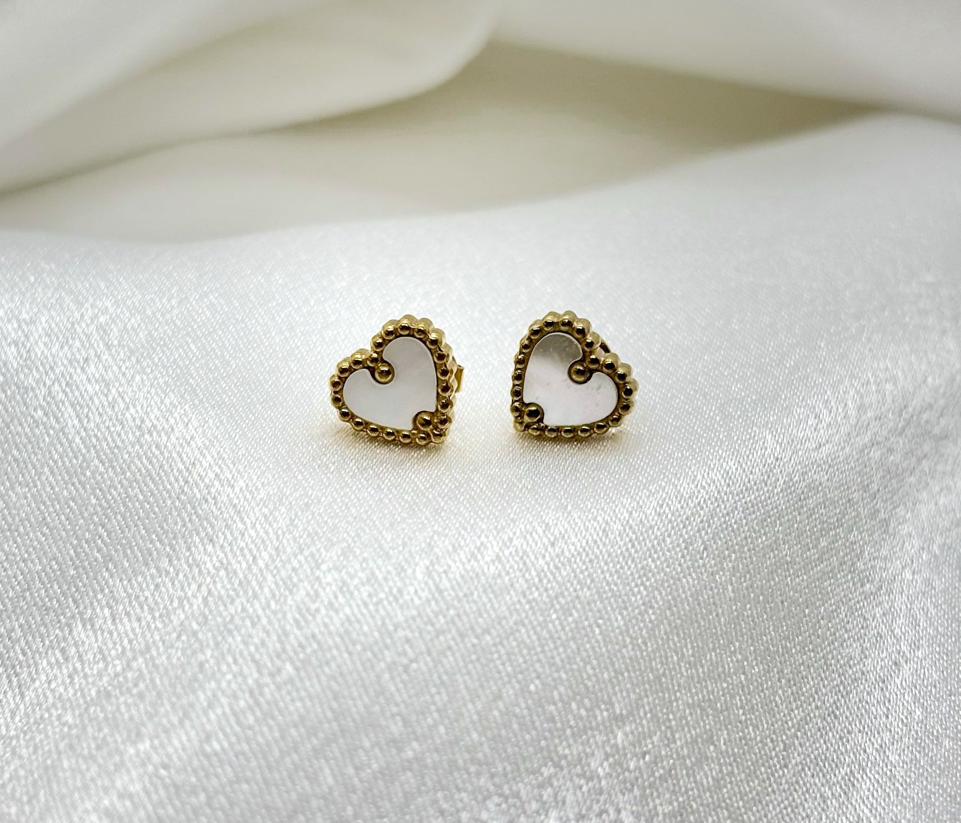 Petites boucles d’oreilles dorées chic coeur nacré en forme de cœur fines et élégantes sur tissu satiné blanc